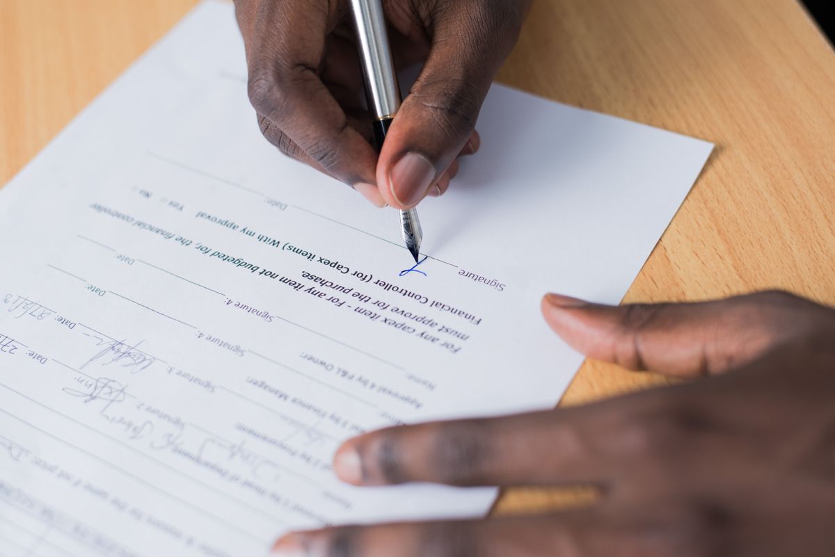 Hand signing a document with a pen on a wooden table.